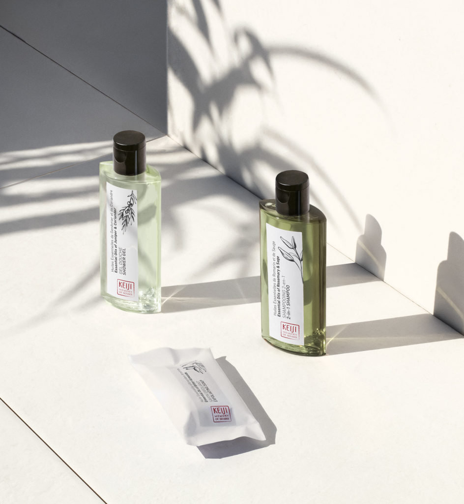 Zwei Flaschen Haarpflegeprodukte stehen auf einer weißen Fläche und werfen Schatten. Eine Flasche ist durchsichtig und grün, daneben liegt eine Packung Tücher.