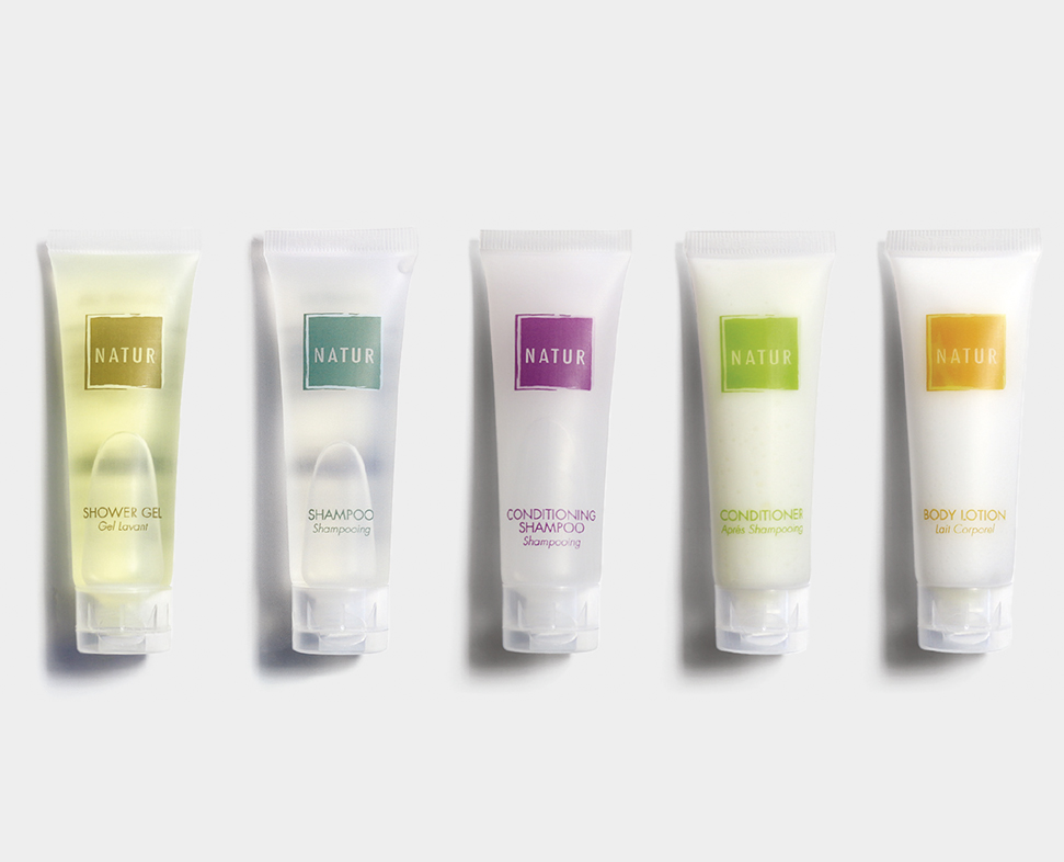 Cinque tubetti di prodotti per la cura personale etichettati come gel doccia, shampoo, shampoo balsamo, balsamo e lozione per il corpo, tutti caratterizzati da un design minimalista.