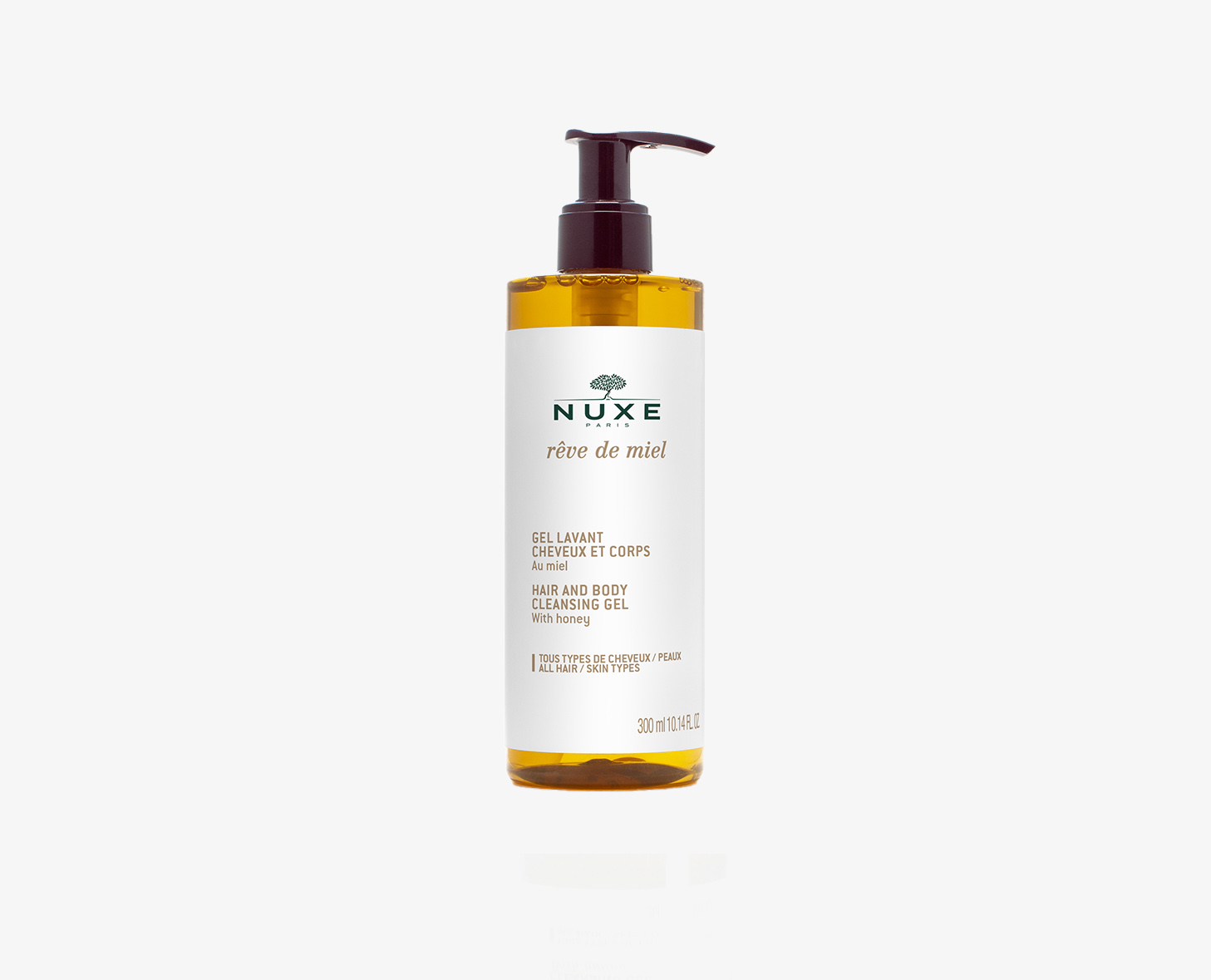 Um frasco de gel de limpeza para cabelo e corpo NUXE Rêve de Miel, com um dispensador de bomba e um líquido de cor âmbar. O rótulo é branco com texto preto e um logótipo dourado.