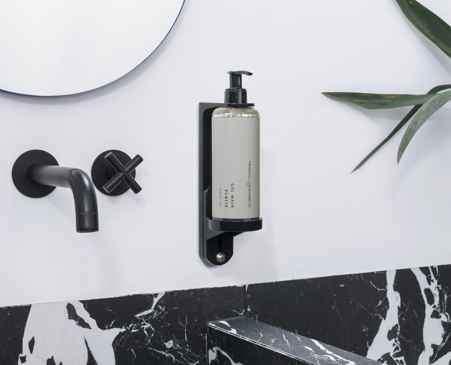 Ein eleganter Flüssigseifenspender, der an einer schwarzen Wand mit einem modernen Wasserhahn und einem runden Spiegel darüber angebracht ist. Der Spender zeichnet sich durch ein minimalistisches Design und eine Flasche in neutraler Farbe aus.