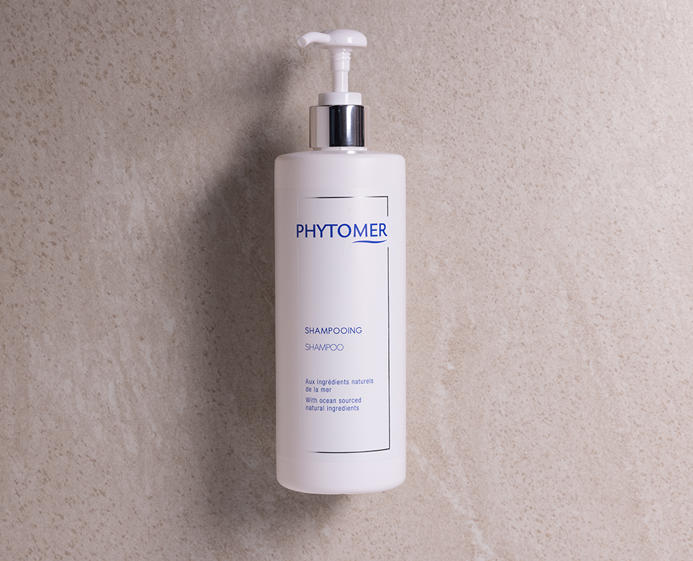 Een witte fles Phytomer met een pompdispenser en een eenvoudig, modern etiket. De fles staat tegen een lichtgekleurde achtergrond met textuur.