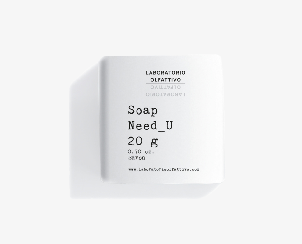 Una piccola confezione di sapone bianco con l'etichetta "Need_U", del peso di 20 grammi e il marchio "Laboratorio Olfattivo".