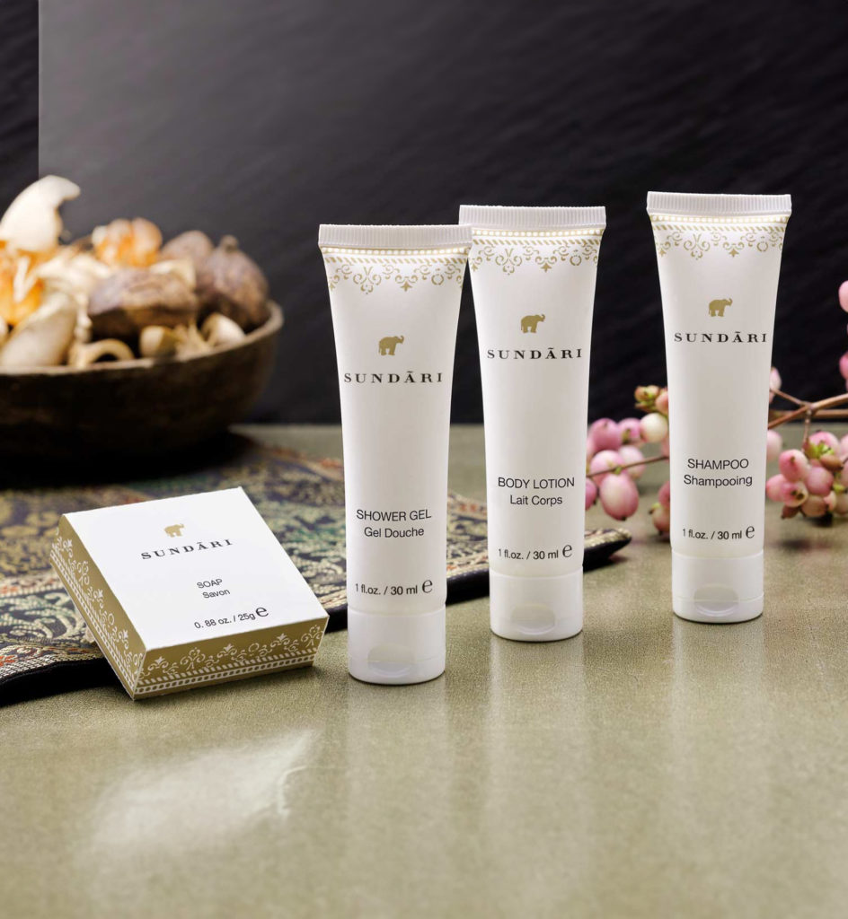 Uma coleção de produtos Sundari , incluindo gel de banho, loção corporal e champô, expostos ao lado de uma caixa decorativa e elementos naturais, como conchas e flores, sobre uma superfície lisa.