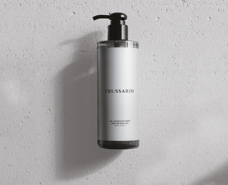 Eine durchsichtige Flasche Trussardi Körper- und Duschgel mit schwarzem Pumpverschluss, präsentiert vor einem strukturierten weißen Hintergrund.