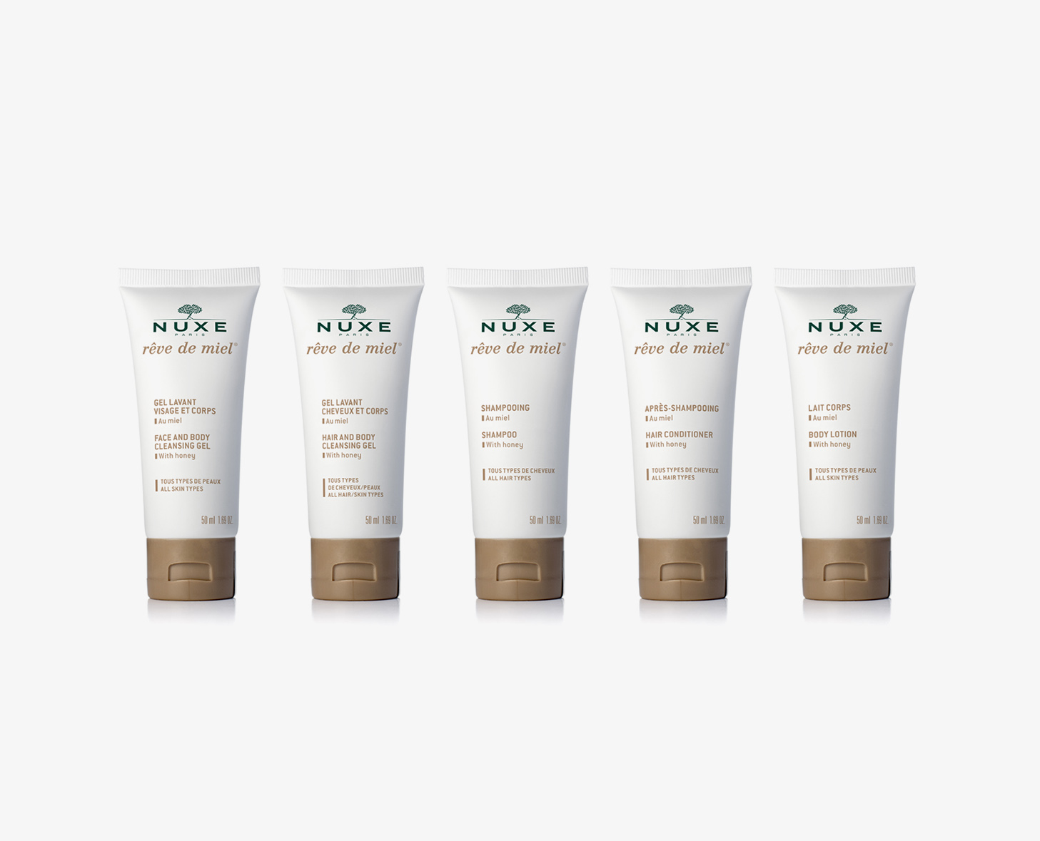 Cinco tubos de produtos para a pele NUXE Rêve de Miel, incluindo gel de banho, gel de limpeza para rosto e corpo, champô, condicionador e loção corporal, dispostos em fila.