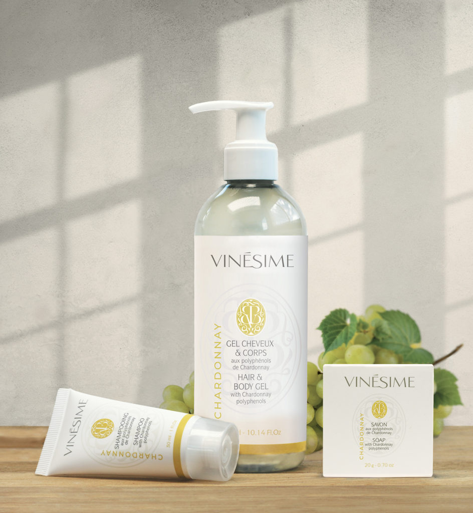 Uma coleção de produtos de higiene pessoal Vinesime, incluindo um gel para cabelo e corpo, um tubo de creme e um sabonete, exibidos com um fundo de luz e elementos de videira.
