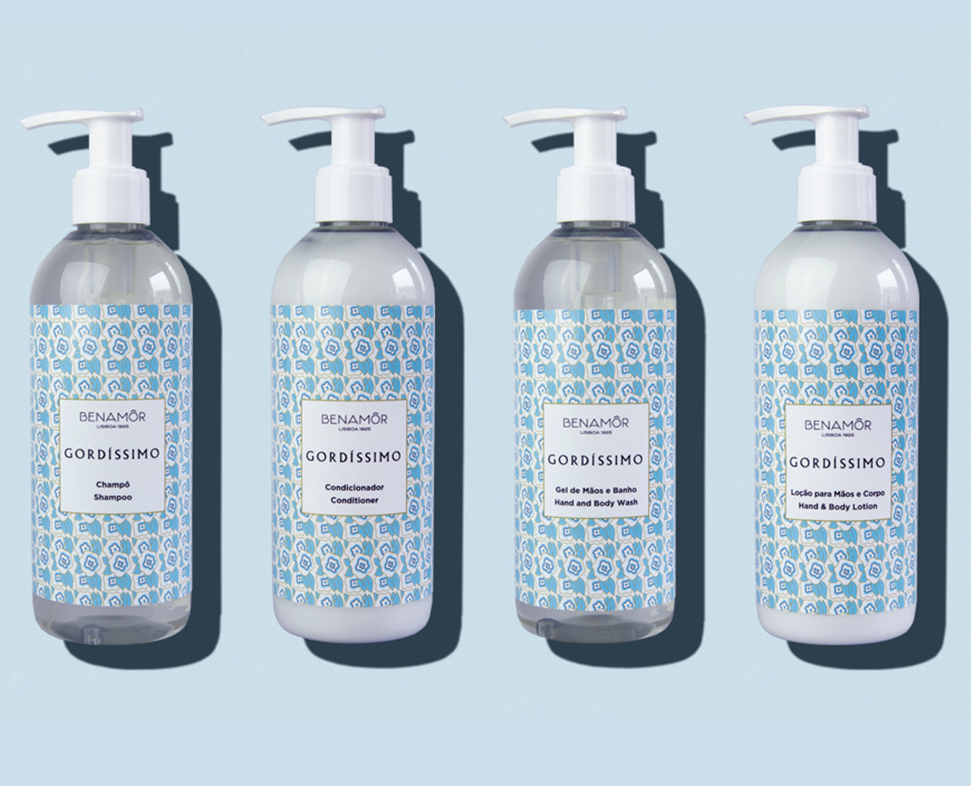 Quattro flaconi di prodotti Benamor Gordissimo e corpo Benamor Gordissimo , tra cui shampoo, balsamo e lozione, esposti su uno sfondo azzurro. Ogni flacone presenta un'etichetta decorata nei toni del blu e del bianco.