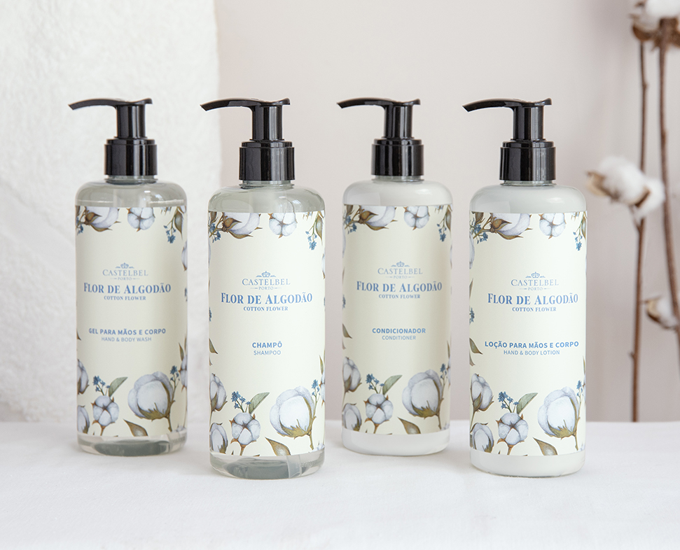 Quatro frascos de produtos de higiene pessoal da marca «Castebel» com a etiqueta «Flor de Algodão», incluindo champô, condicionador, gel de banho e loção corporal, expostos contra um fundo neutro.