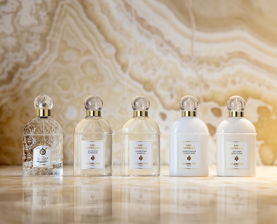 Uma linha de elegantes frascos de perfume dispostos em fila, com várias formas e designs, contra um fundo marmorizado.
