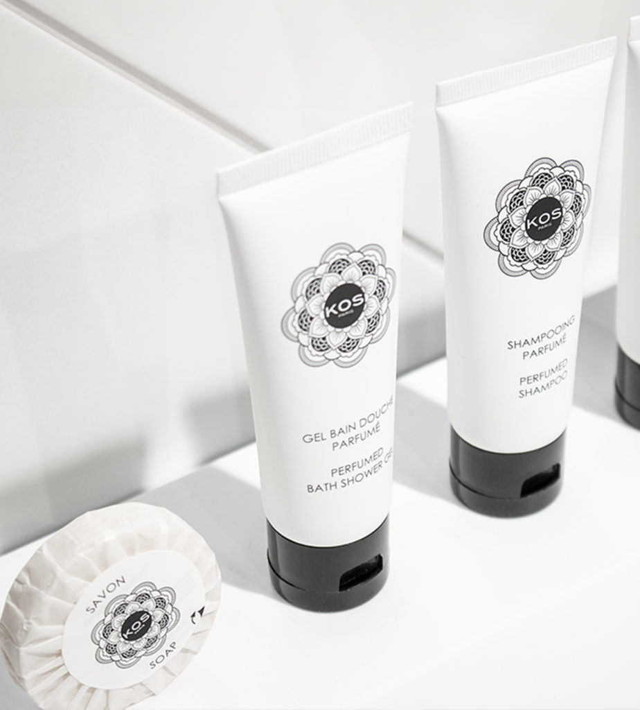 Uma exposição organizada de produtos de higiene pessoal, incluindo pequenos tubos de gel de banho e champô, ao lado de uma barra redonda de sabonete, todos com embalagens minimalistas brancas e rótulos decorativos pretos.