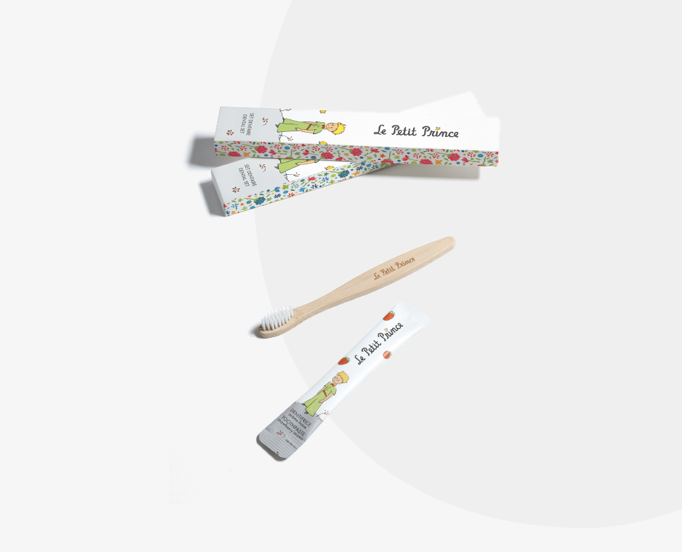 Eine Bambuszahnbürste mit einem hellen Griff und weichen Borsten, zusammen mit einer bunten Verpackung mit Illustrationen zum ThemaLe Petit Prince“.