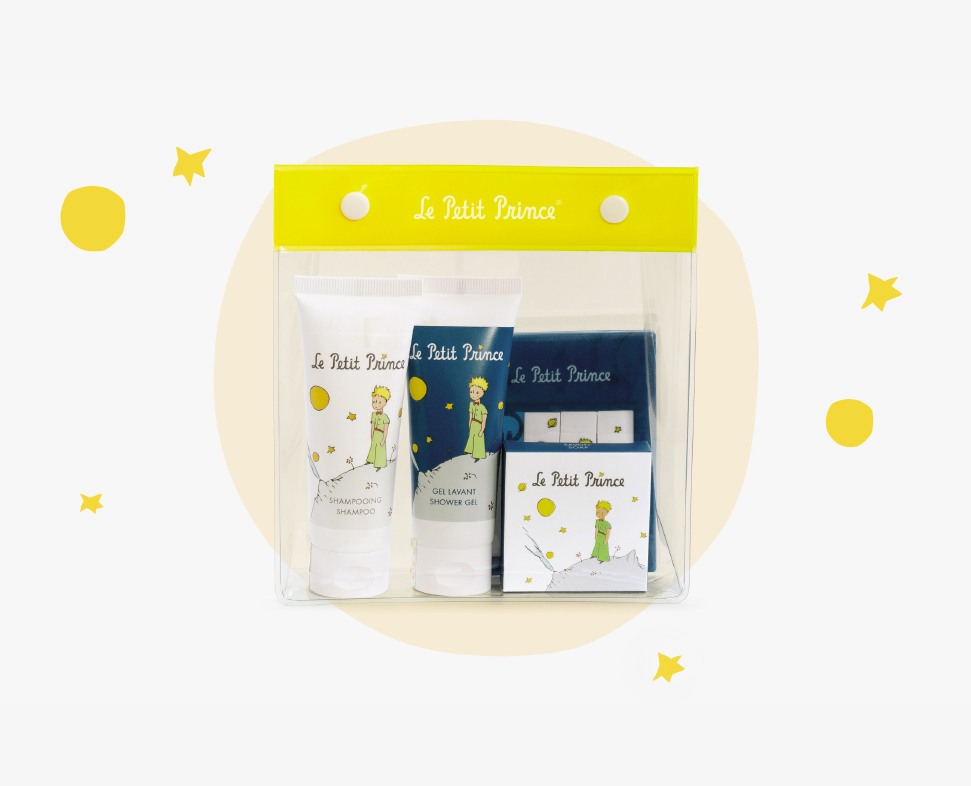 Eine durchsichtige Plastiktüte mit drei Toilettenartikeln Le Petit Prince , darunter Shampoo, Duschgel und eine kleine Schachtel, alles vor einem weißen Hintergrund mit gelben Sternen.