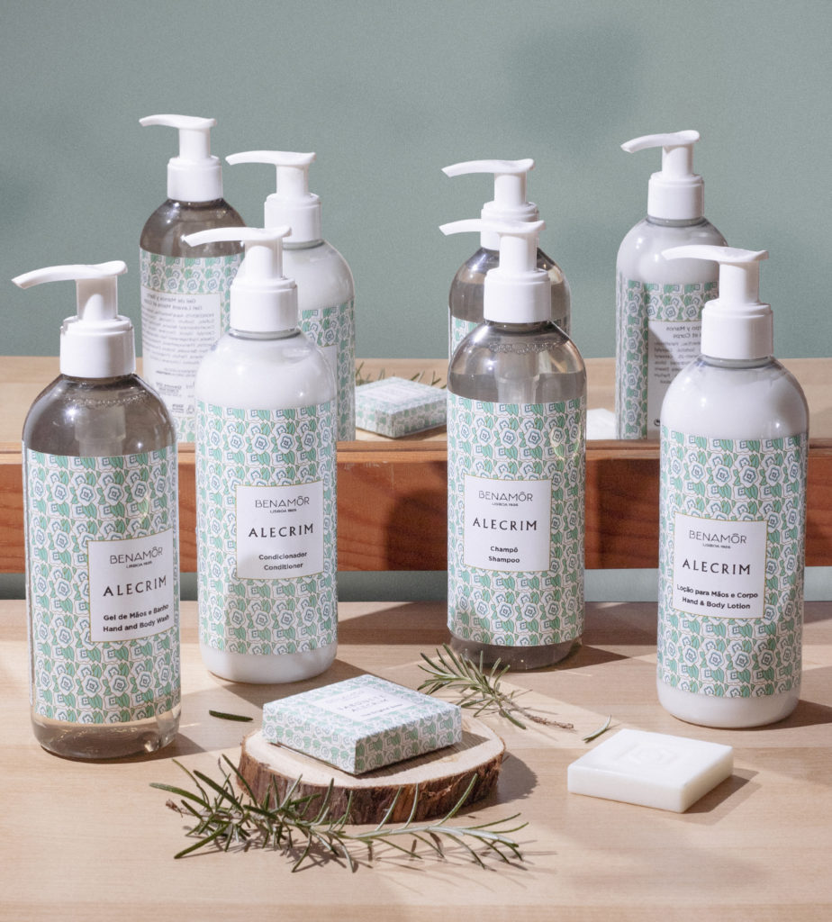 Uma coleção de produtos aromáticos para a pele com rótulos verdes e brancos, expostos sobre uma superfície de madeira com um sabonete e ramos de alecrim fresco.