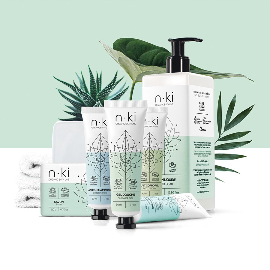Eine Kollektion biologischer Hautpflegeprodukte von n:ki, darunter Shampoo, Duschgel und Seife, ästhetisch arrangiert vor einem Hintergrund aus grünen tropischen Blättern.
