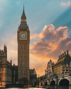 Un'alta torre dell'orologio, conosciuta come Big Ben, si staglia contro un cielo colorato al tramonto, con edifici storici e un fiume in primo piano.