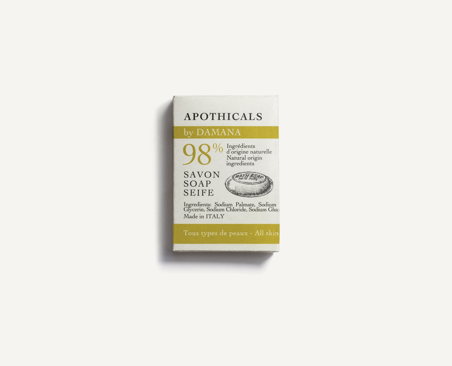 Um sabonete embalado numa caixa minimalista com texto indicando que contém 98% de ingredientes naturais, rotulado como «Apothicals by Damana» e informando que é fabricado na Itália.
