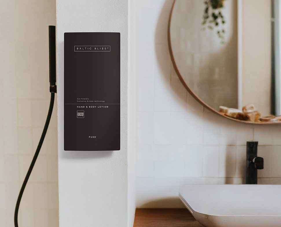 Ein eleganter schwarzer Lotionsspender mit der Aufschrift „BALTIC BLISS“ ist an einer weißen Wand neben einem modernen Waschbecken und Wasserhahn in einem Badezimmer angebracht.