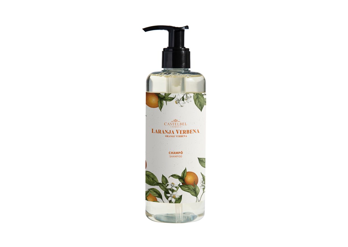 Una bottiglia di shampoo in plastica trasparente con l'etichetta "Laranja Verbena" e un motivo decorativo con elementi floreali arancioni e bianchi. La bottiglia è dotata di un erogatore a pompa nero sulla parte superiore.