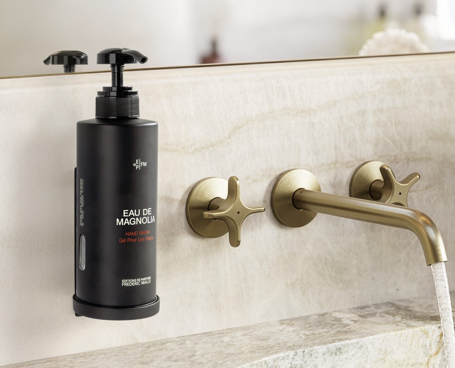 Un flacone cilindrico nero con pompa etichettato "Eau de Magnolia" è appoggiato su un lavandino in marmo con eleganti rubinetti in ottone in un bagno moderno.