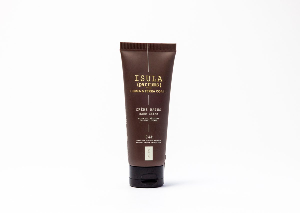 Un tubetto marrone di crema per le mani con l'etichetta "ISULA", la scritta "Crème Mains" e l'elenco degli ingredienti. Il tubetto è ripreso su uno sfondo neutro.