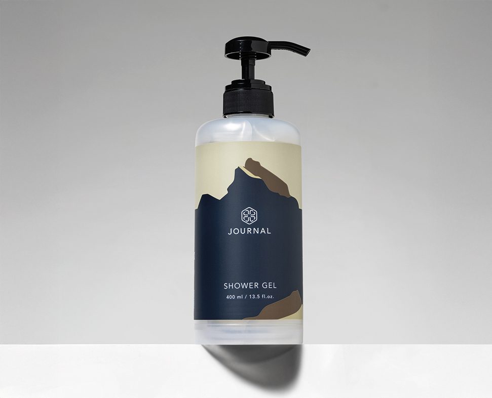 Flacone trasparente di gel doccia con erogatore a pompa, caratterizzato da un'etichetta dal design minimalista che include immagini di montagne e la scritta "JOURNAL GEL".