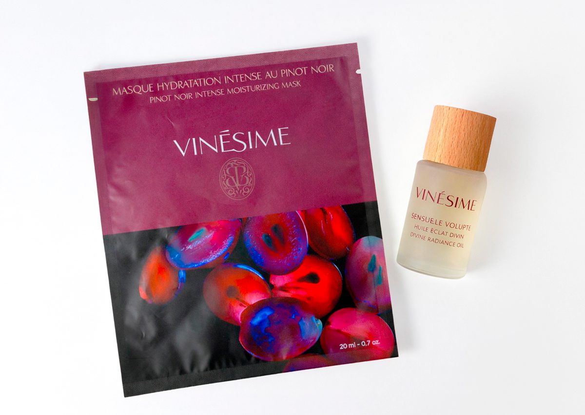 Uma bolsa de Máscara Hidratante Intensa Vinésime Noir juntamente com um frasco de Óleo Radiante Vinésime Volupté, ambos com embalagens vibrantes e coloridas.
