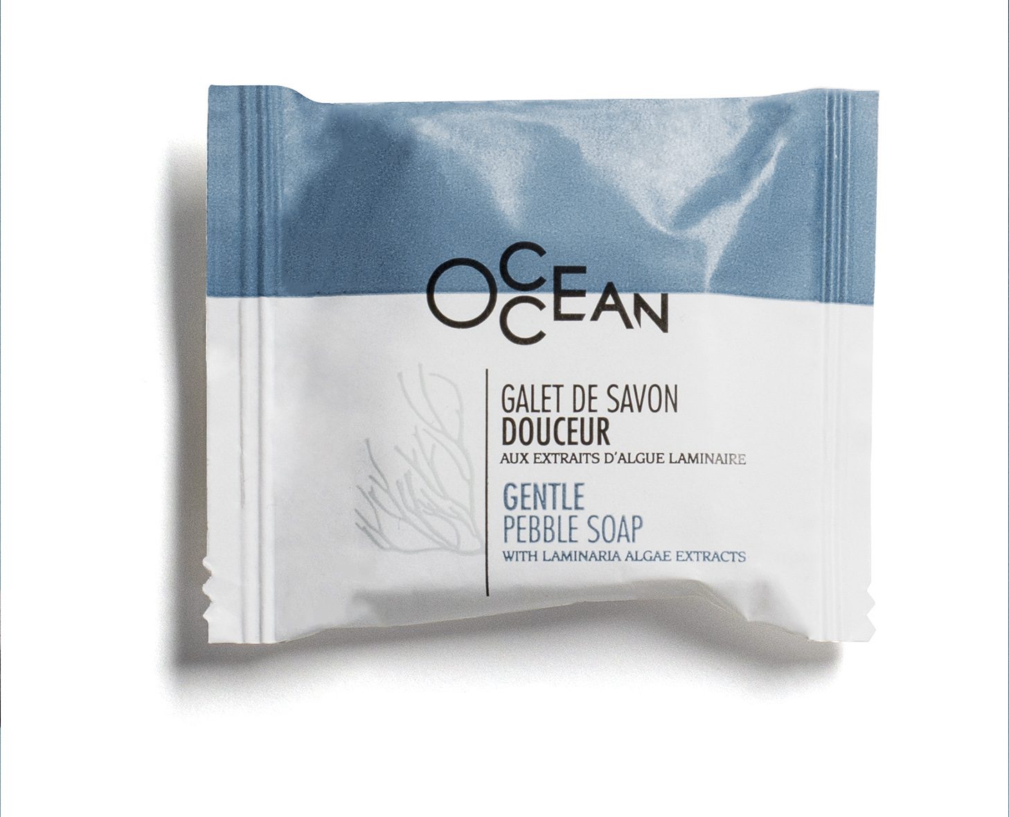 Una confezione di sapone delicato a forma di ciottolo con la scritta "Ocean" e un disegno blu e bianco, con testo in francese e inglese. Il sapone contiene estratti di alghe Laminaria.