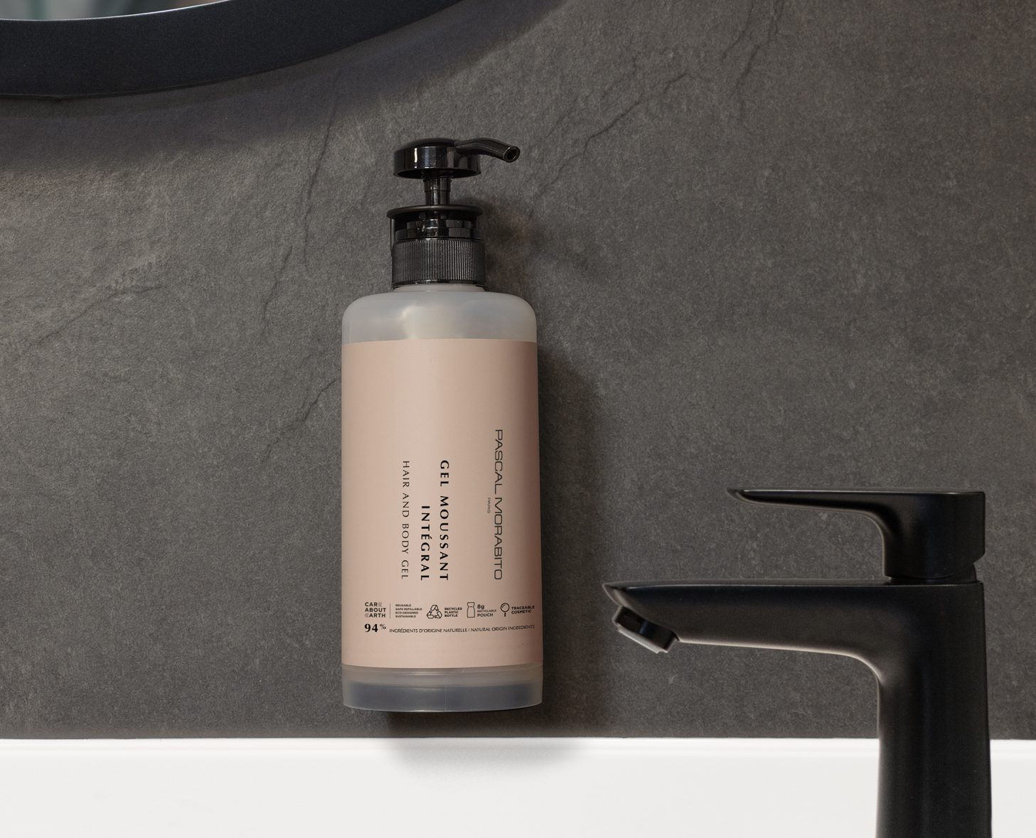 Eine beige Pumpflasche mit der Aufschrift „Gel Moisturizer” hängt an einer dunklen Steinwand neben einem eleganten schwarzen Wasserhahn.