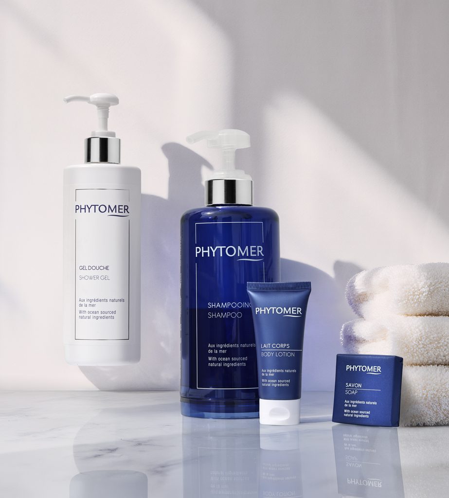 Een collectie Phytomer van Phytomer , waaronder douchegel, shampoo, bodylotion en zeep, uitgestald op een marmeren oppervlak met witte handdoeken.