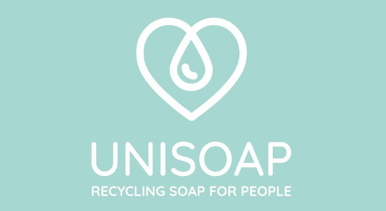 Logo di Unisoap raffigurante un cuore con all'interno una goccia d'acqua, accompagnato dal testo "RECYCLING SOAP FOR PEOPLE" (Ricicliamo il sapone per le persone) sotto di esso. Lo sfondo è di un delicato colore turchese.