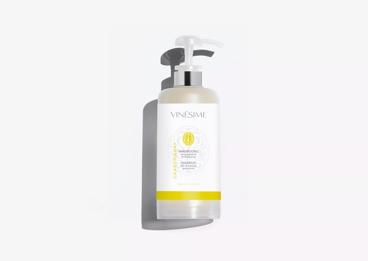 Um frasco de champô Vinésime com dispensador, com um design elegante e um rótulo branco com detalhes em amarelo. O champô é apresentado contra um fundo branco liso.