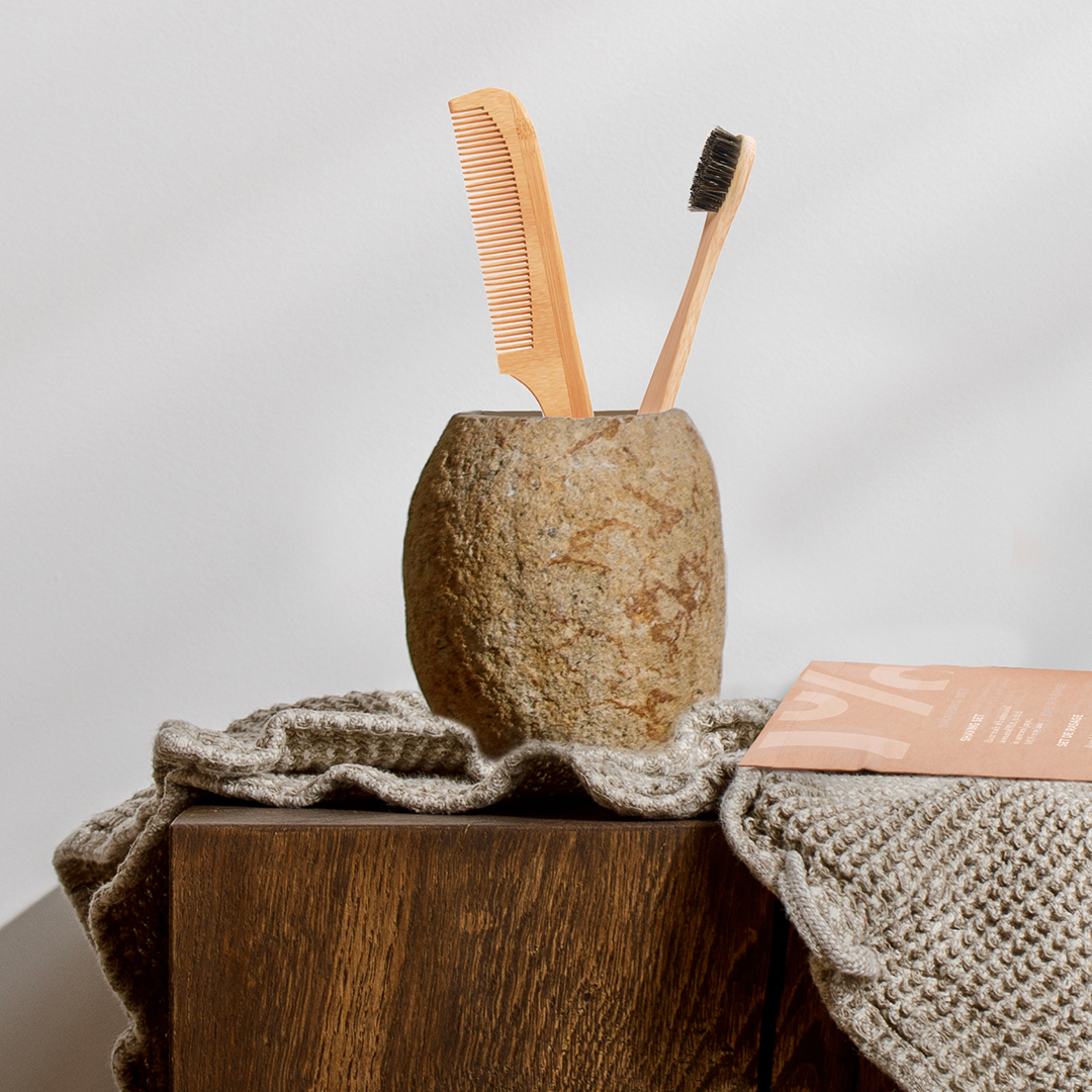 Umweltfreundliche Bambuszahnbürste und Holzkamm in einem Steinbecher auf einer Holzunterlage mit Naturstoff
