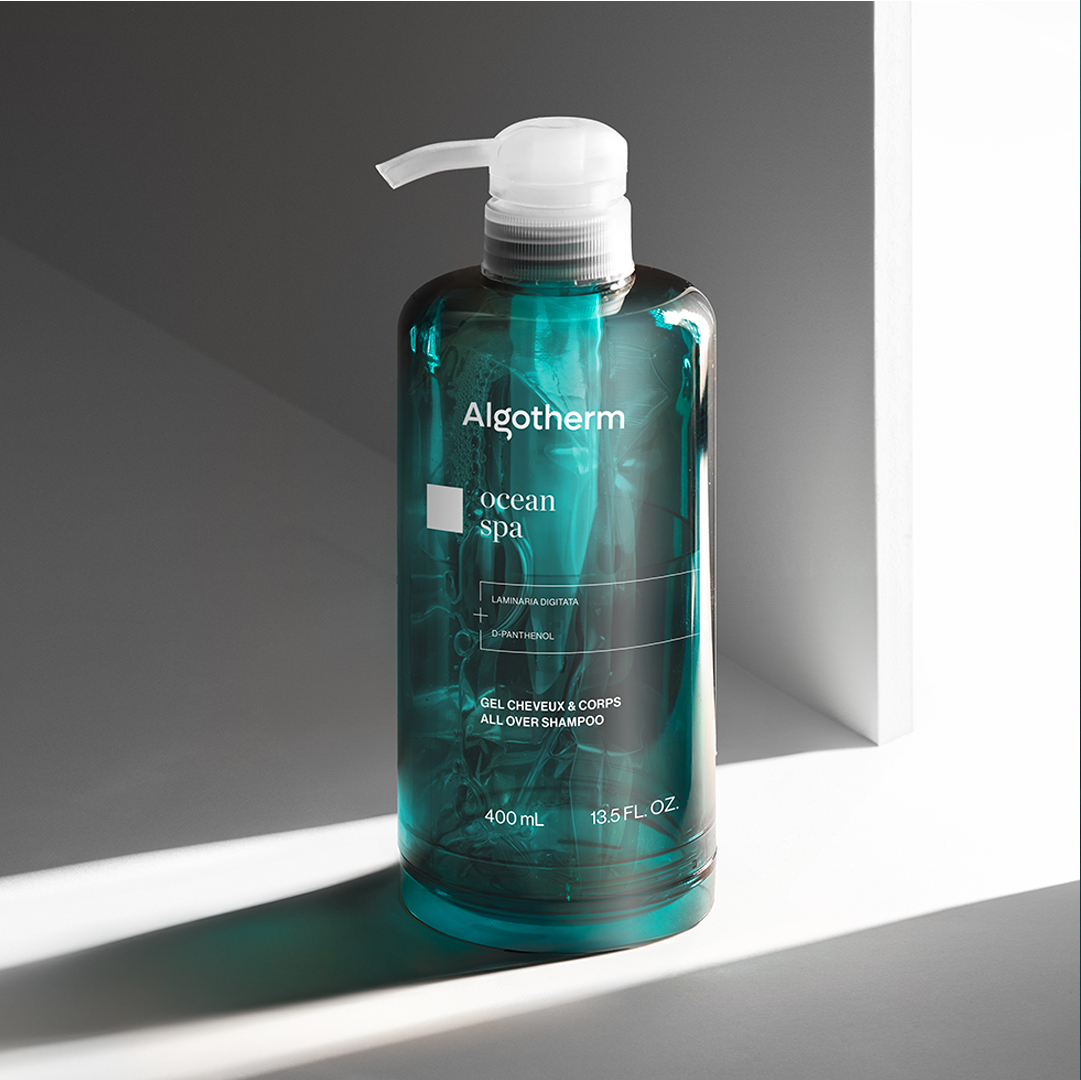 Algotherm Ocean Spa All-Over-Shampoo in einer transparenten, blaugrünen Pumpflasche, präsentiert in sanftem Licht vor einem minimalistischen Hintergrund