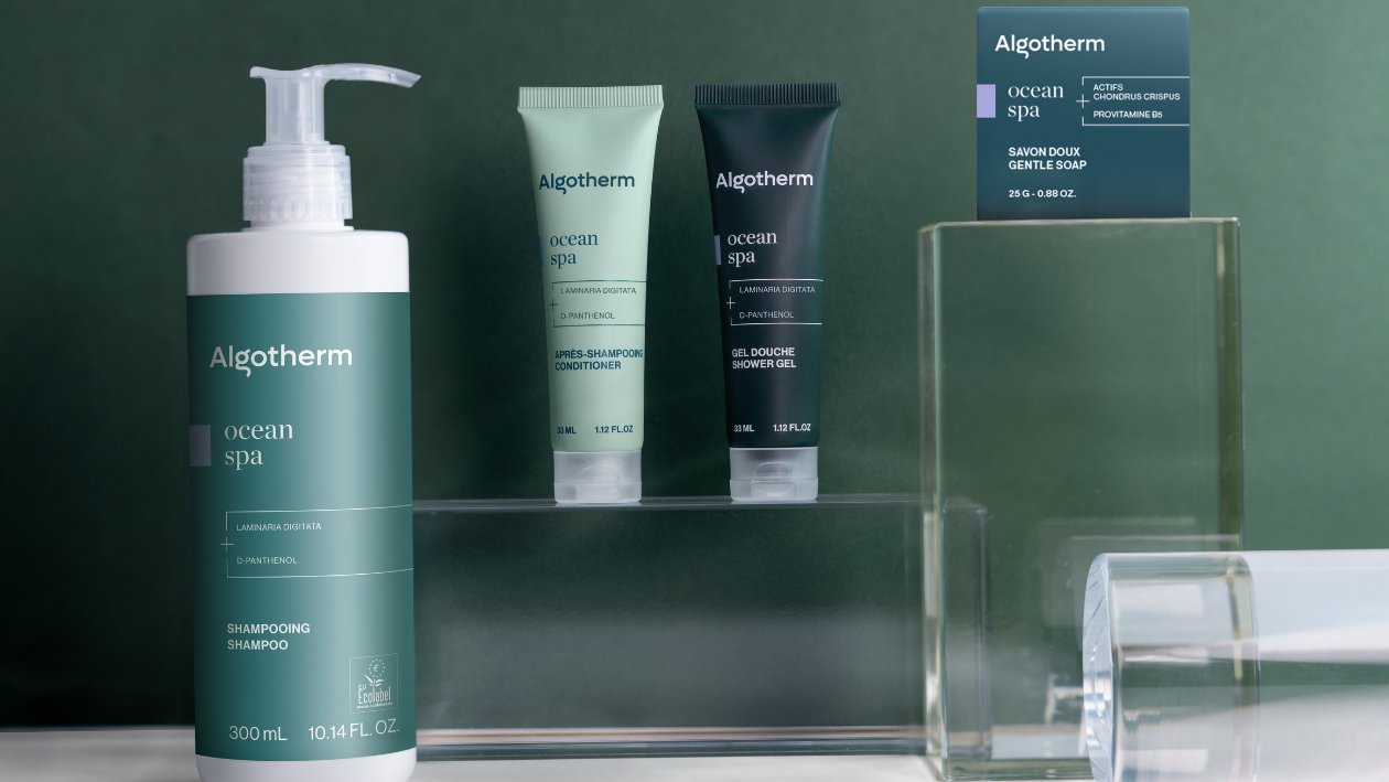 Algotherm Die Ocean Spa-Produktreihe mit Shampoo, Spülung, Duschgel und Seife, präsentiert auf Glasständern vor grünem Hintergrund