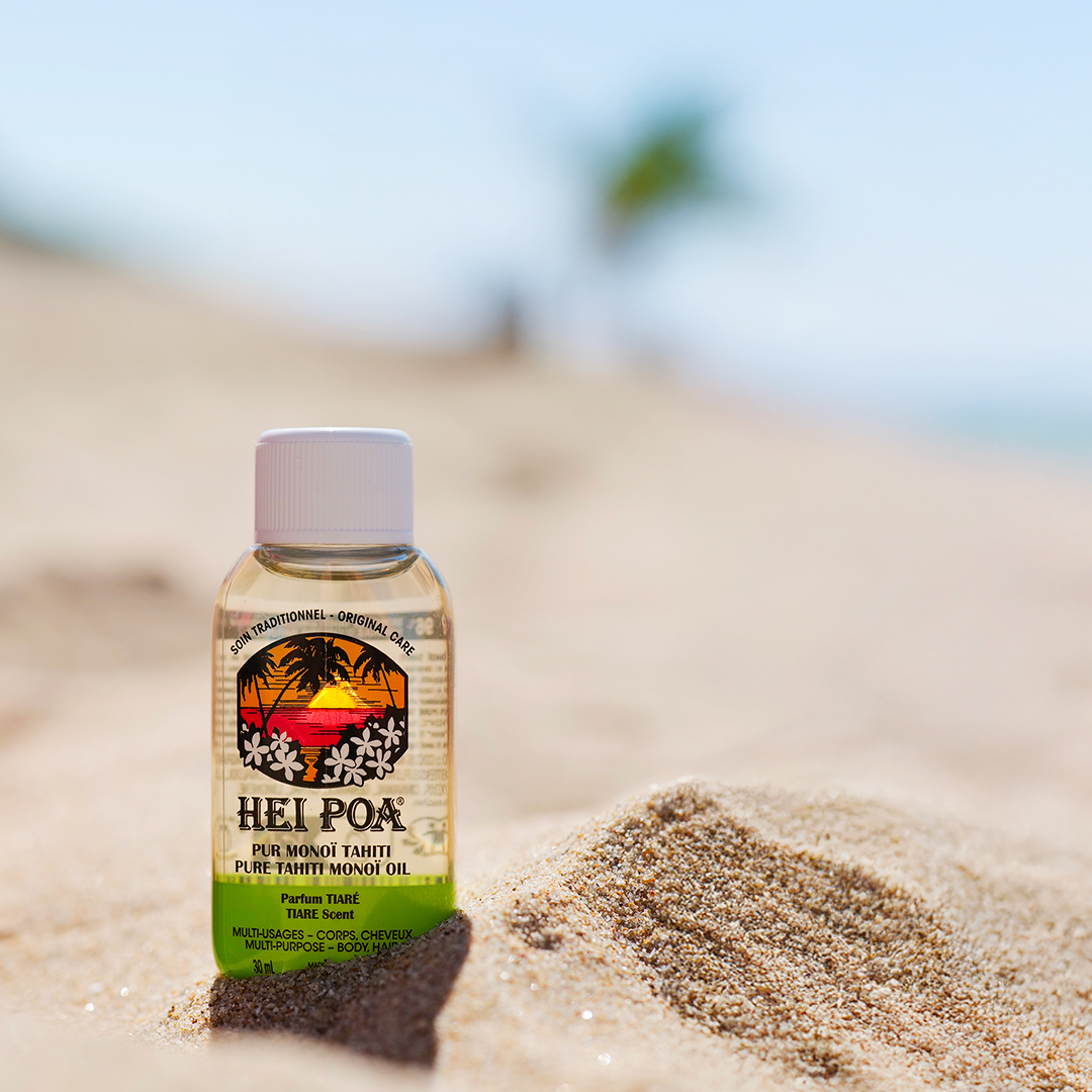 Hei Poa Monoi-Ölflasche auf dem Sandstrand vor einem verschwommenen tropischen Hintergrund