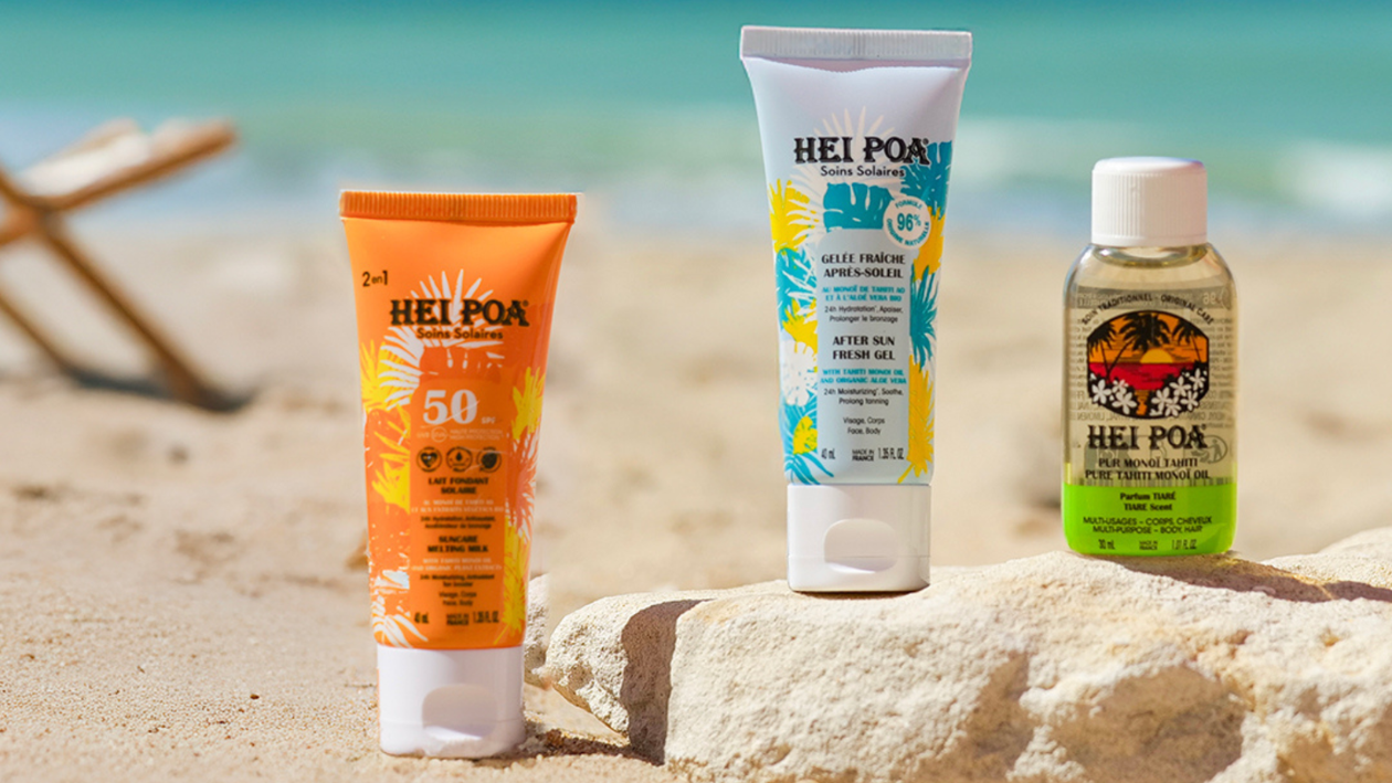 Hei Poa Sonnenschutzprodukte, darunter Sonnencreme mit LSF 50, After-Sun-Gel und Monoi-Öl, ausgestellt auf dem Sand am Strand