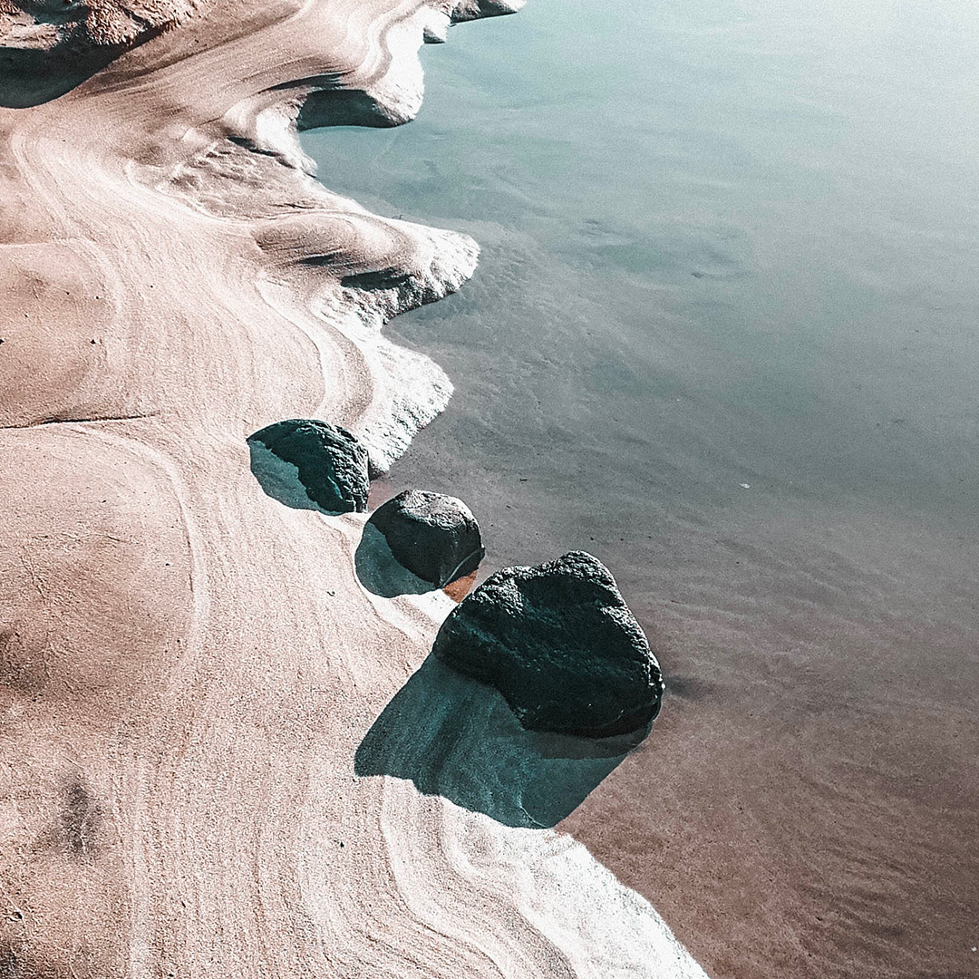Rocky shoreline with smooth sand patterns and calm water, viewed from above