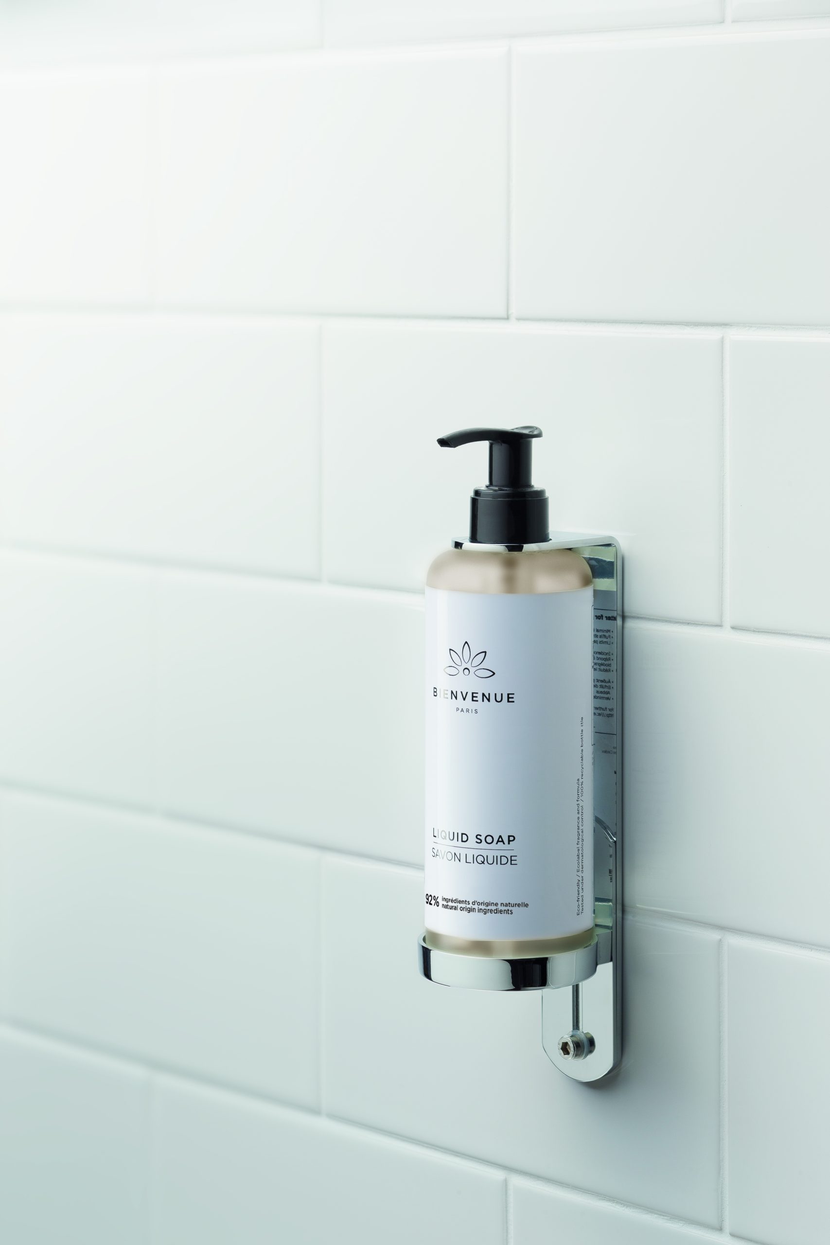 Bienvenue Flüssigseifenflasche von Paris an einer weiß gefliesten Wand in einem minimalistischen Badezimmer.