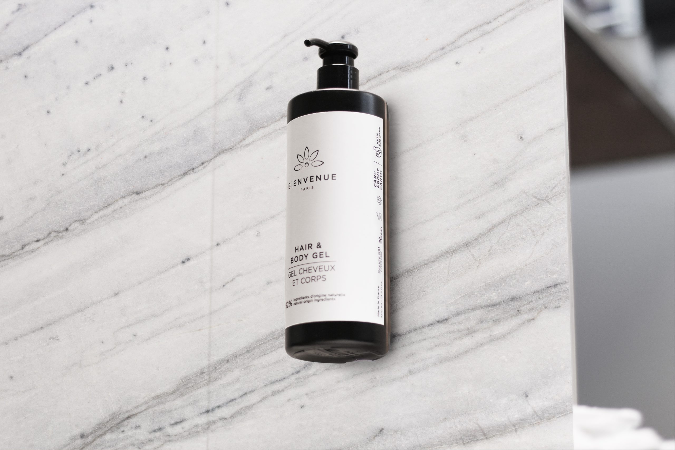 Bienvenue Eine Flasche Paris Haar- und Körpergel an einer hellen Marmorwand in einem klaren, minimalistischen Badezimmer.