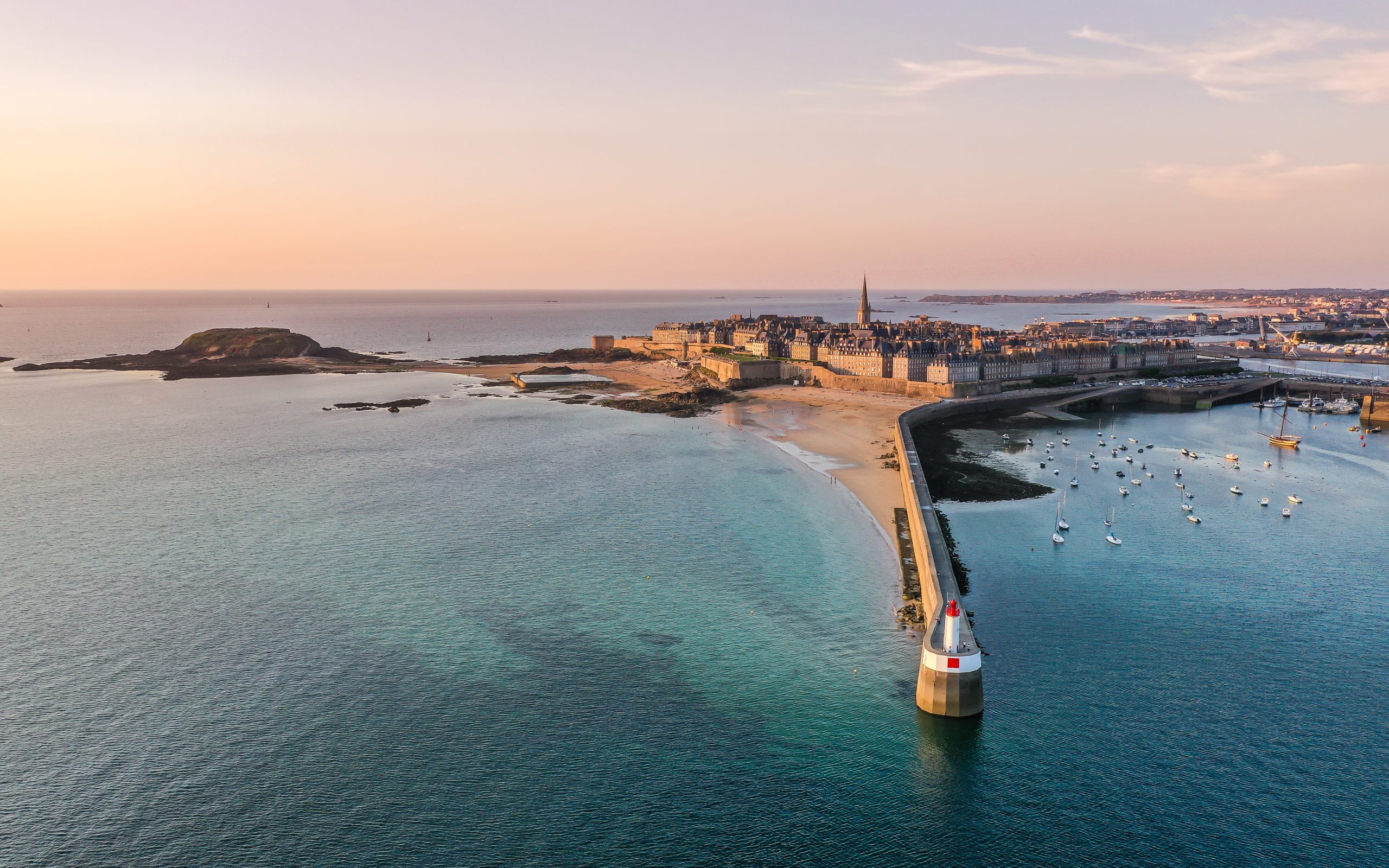Luftaufnahme der Küste von Saint-Malo mit Stadtmauer, Hafen und Leuchtturm bei Sonnenuntergang.