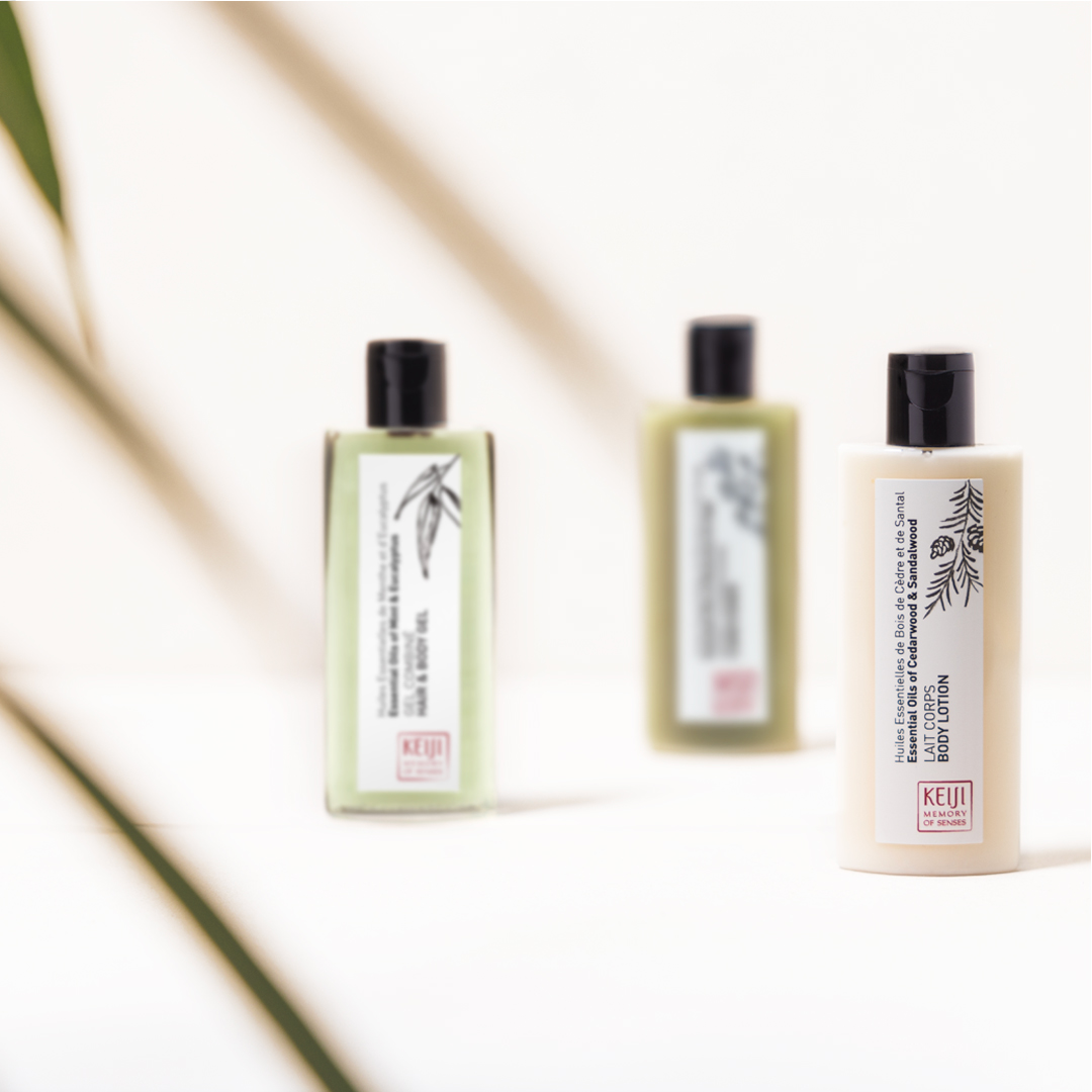 Keiji Memory of Senses Haar- und Körpergel in einer grünen, transparenten Flasche mit schwarzer Pumpe, platziert auf einer weißen Fläche, auf die starkes Sonnenlicht Schatten wirft und so das frische, von der Natur inspirierte Design hervorhebt.