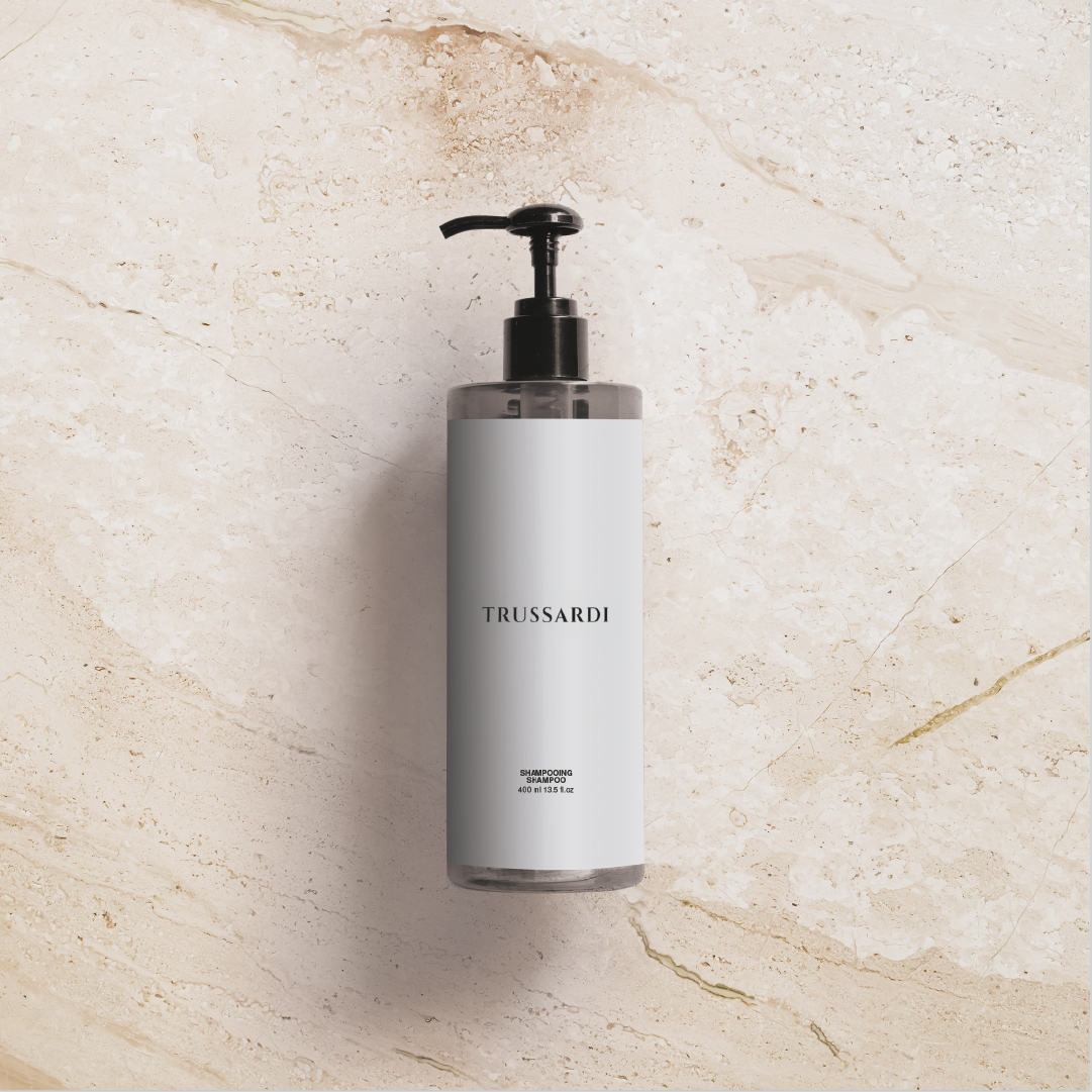 Trussardi Shampooflasche mit schwarzer Pumpe, zentriert auf einem beigen Marmorhintergrund, mit einem minimalistischen weißen Etikett und sanften Schatten, die das klare, elegante Design unterstreichen.