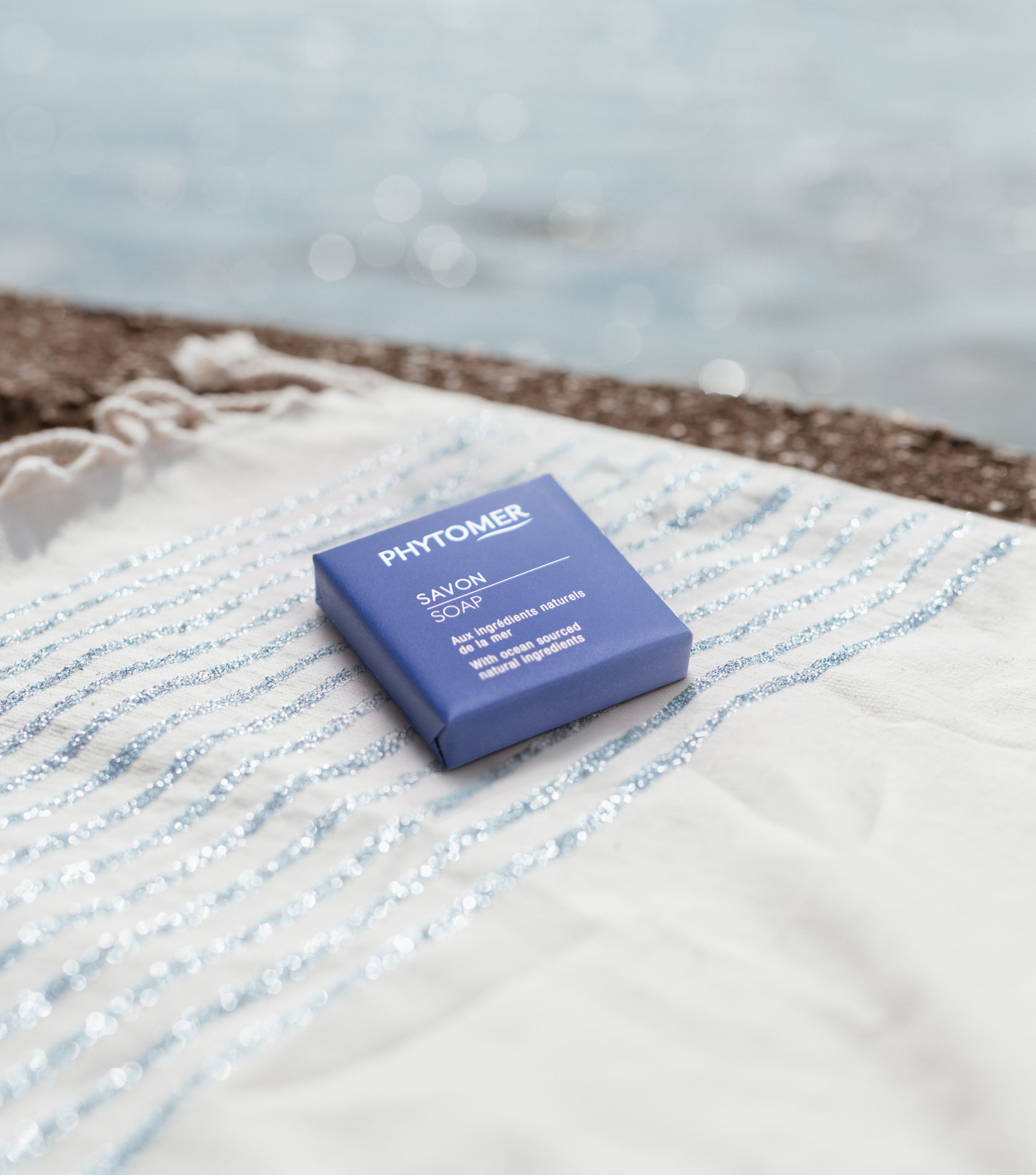 Phytomer eine verpackte Seife, die auf einem gestreiften Strandtuch am Meer liegt.