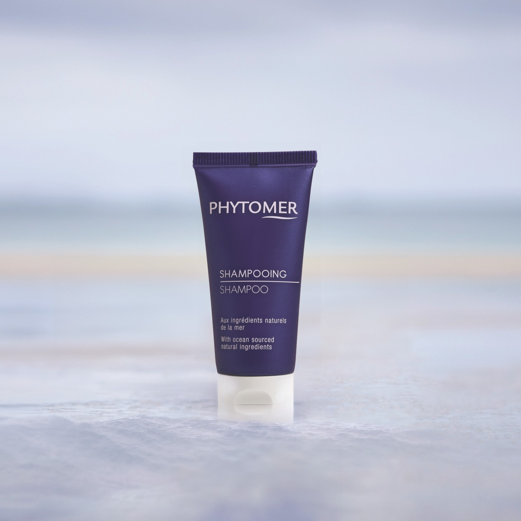 Phytomer Shampoo in Reisegröße in einer Tube, stehend in seichtem Wasser vor einem sanften Strandhintergrund.