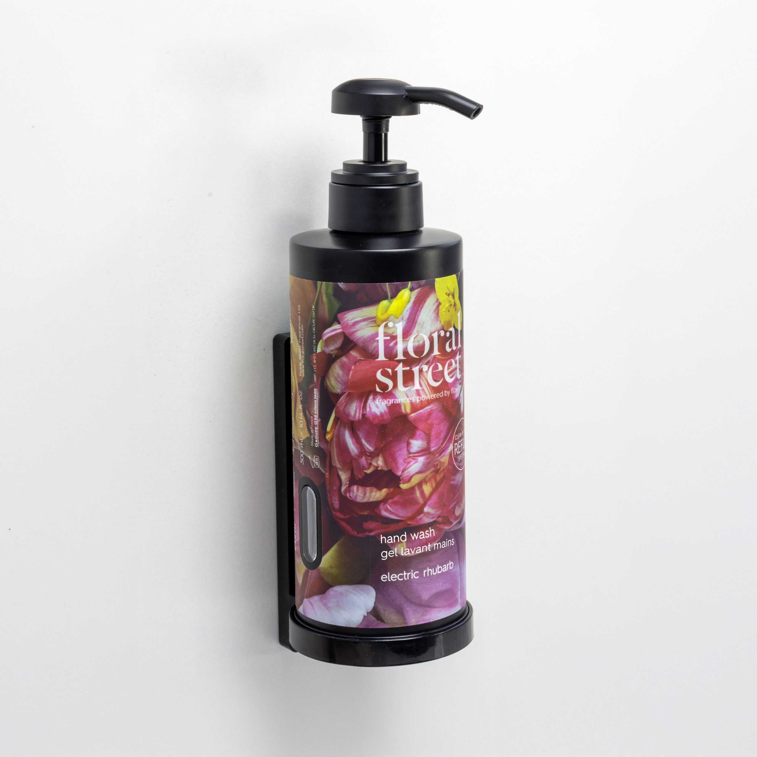 Floral Street Sabonete líquido «Electric Rhubarb» num dispensador recarregável de parede com bomba preta, sobre um fundo de parede branco minimalista.