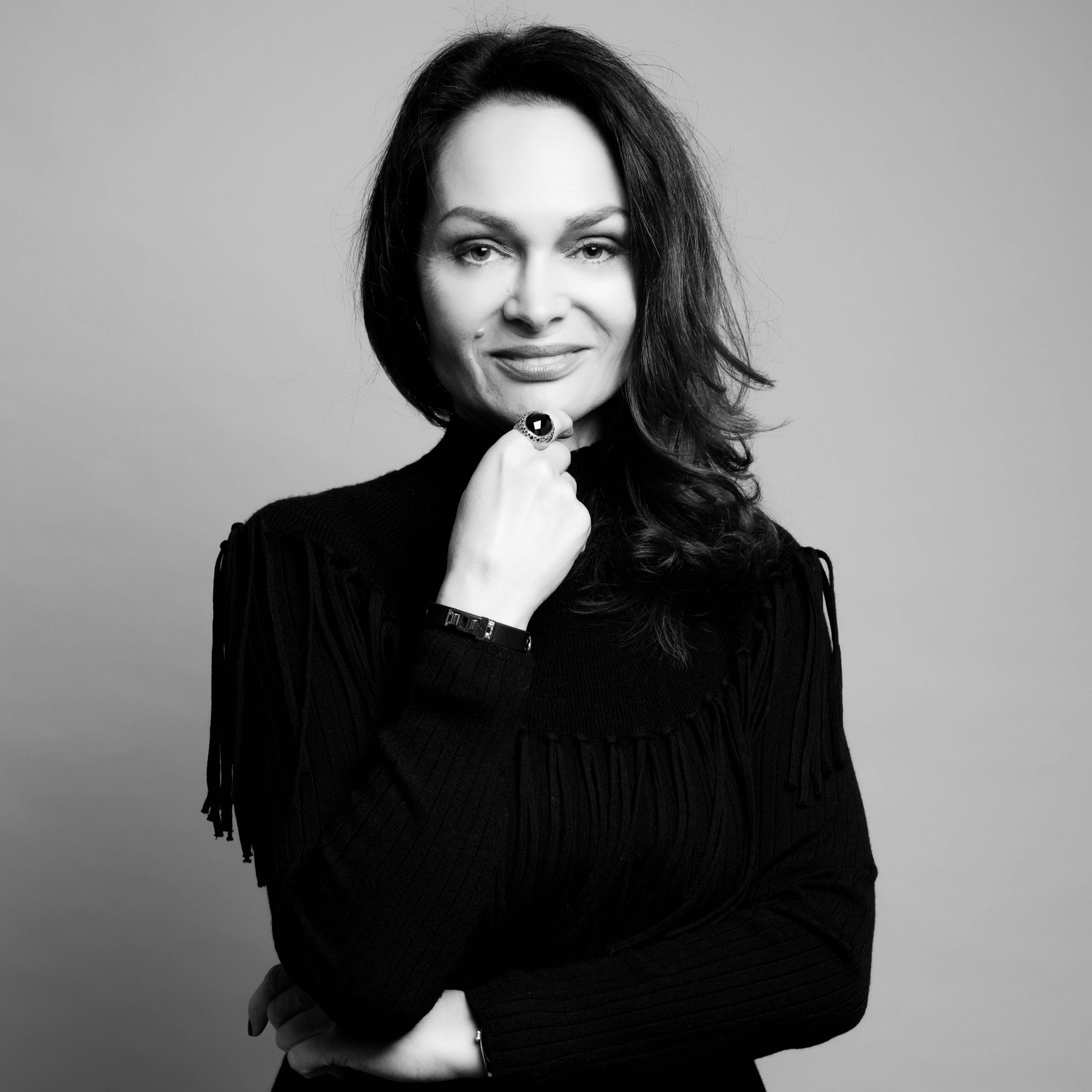 Chrystelle Lannoy’un koyu renkli, yüksek yakalı bir kazak giymiş, tek elini çenesinin altına koymuş halde, düz gri bir arka plan önünde poz verdiği siyah-beyaz stüdyo portresi.