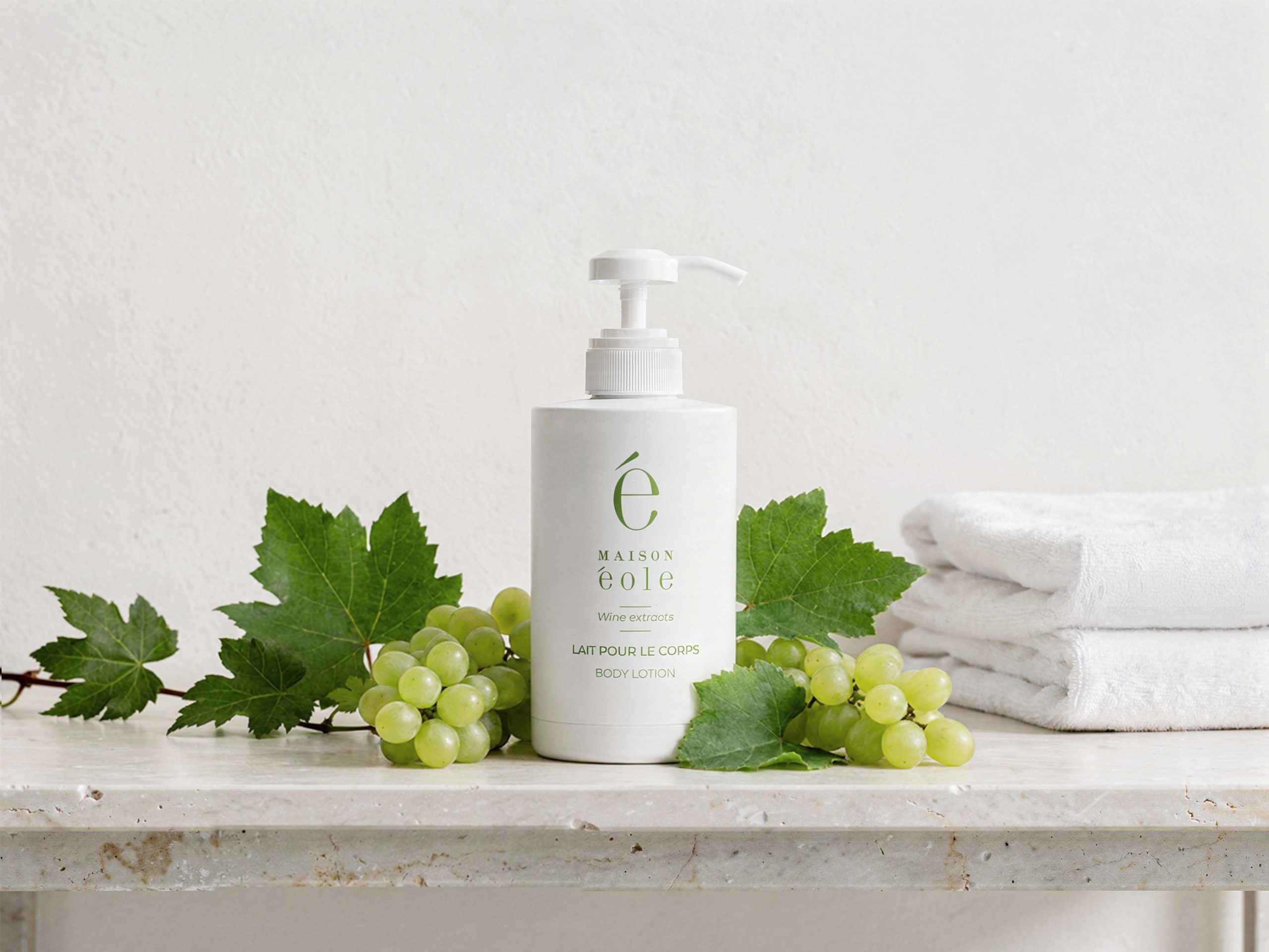 Maison Éole body lotion displayed with fresh grapes and vine leaves on a bathroom countertop.