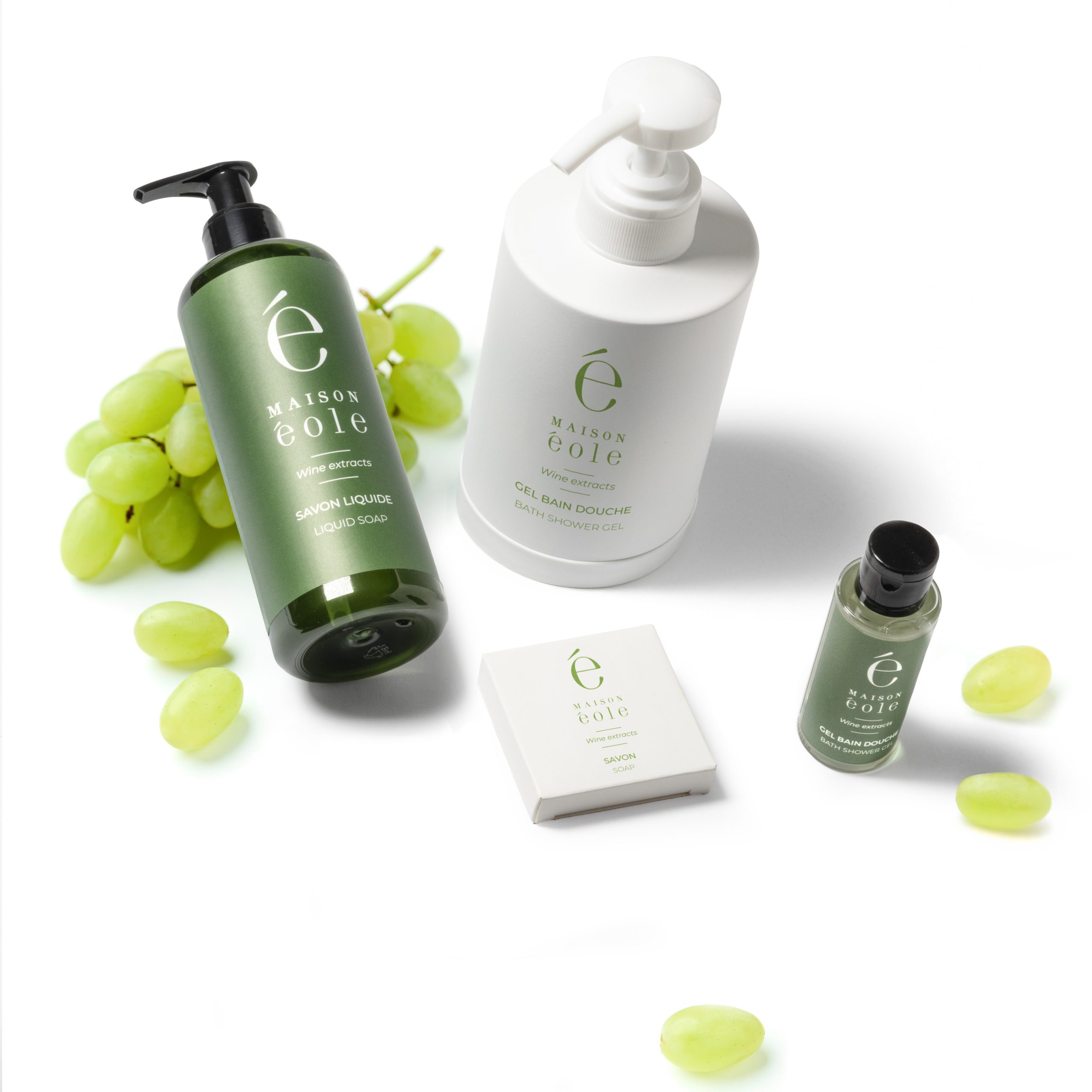 Maison Éole hospitality amenities collection featuring liquid soap, shower gel, soap, and mini toiletries displayed with fresh green grapes.