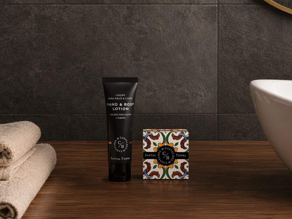 Castelbel Santal Tonka hand and body lotion and soap displayed on a bathroom vanity beside a sink and folded towels.