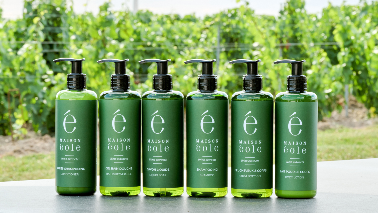 Maison Éole wine-extract body care products displayed in front of a vineyard.